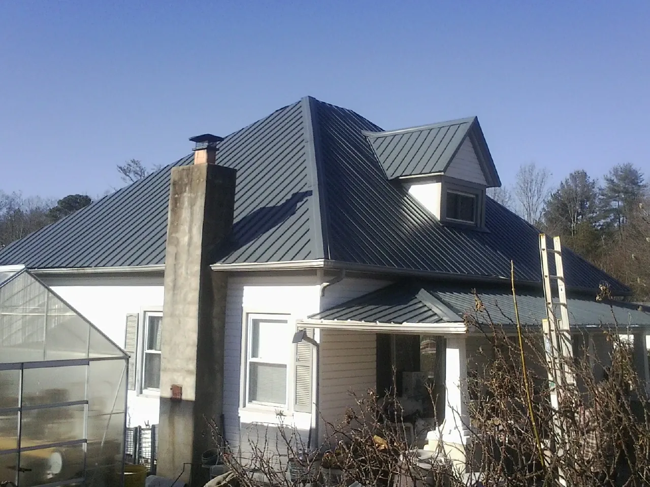Dark blue standing seam metal roof on a white farmhouse with dormer — Slate & Tile Roof Repair by Roofing Brothers in Marthasville