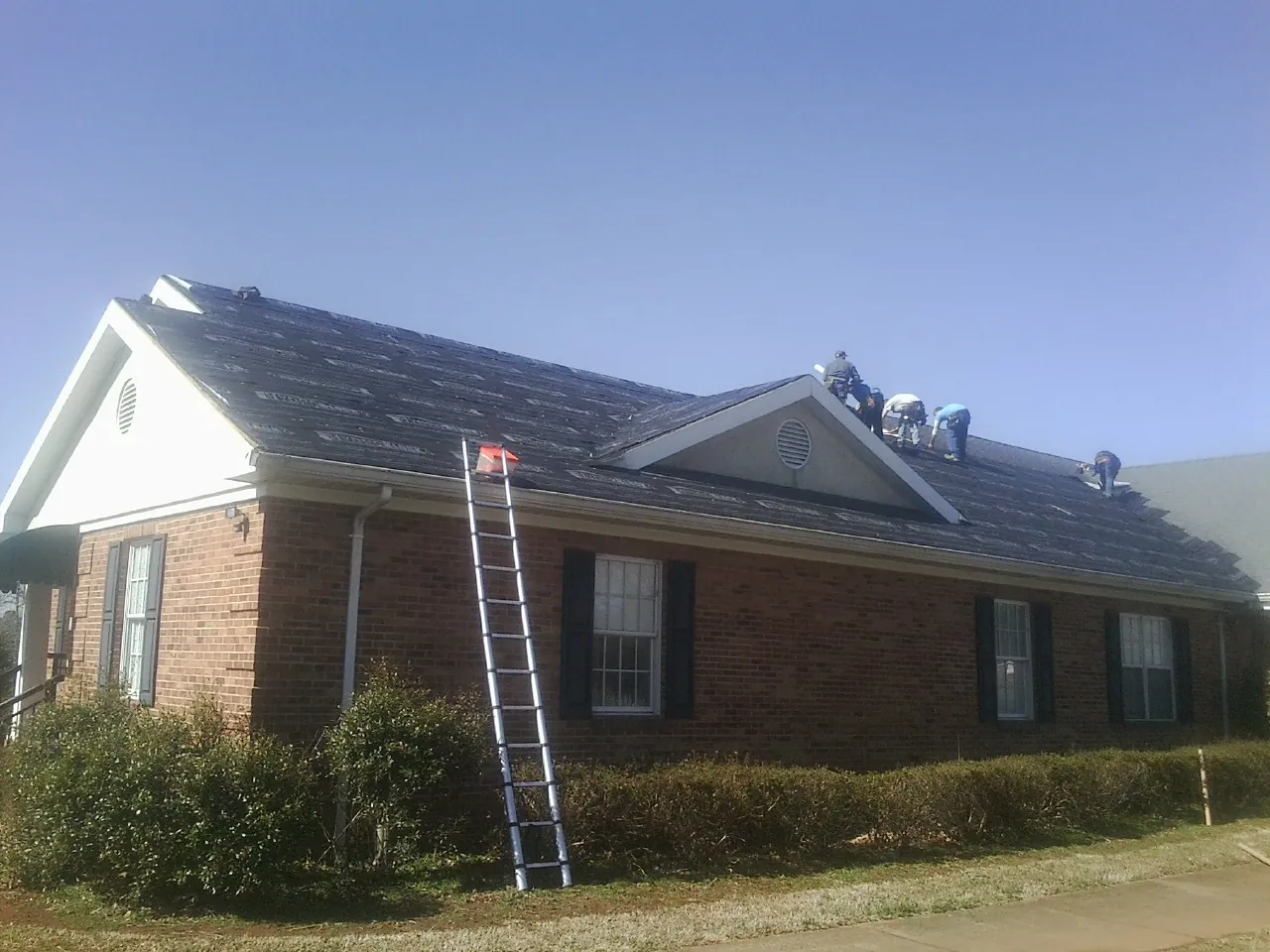 Crew tearing shingles off a brick ranch roof with a ladder set — Metal Roof Repair work by our crew in Marthasville