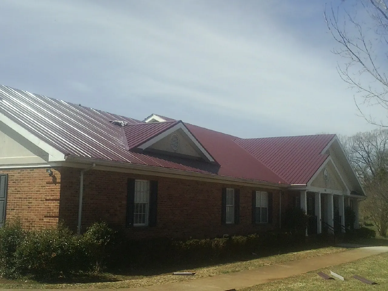 Red metal roof with gabled entries on a long brick building, from a Hail Damage Roof Repair job in Marthasville