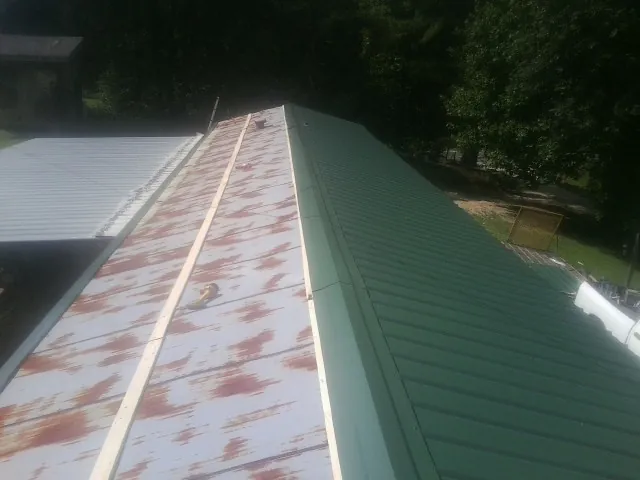 Old rusted panels beside newly installed green metal roofing — Wind Damage Roof Repair by Roofing Brothers in Marthasville