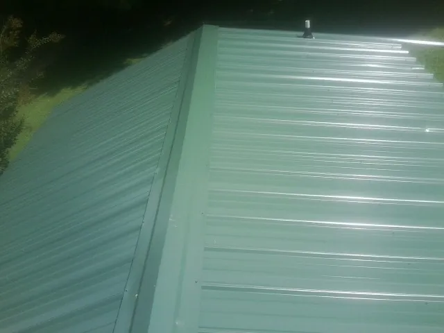 New green metal panels meeting at the ridge of a roof — Flat Roof Repair work by our crew in Marthasville