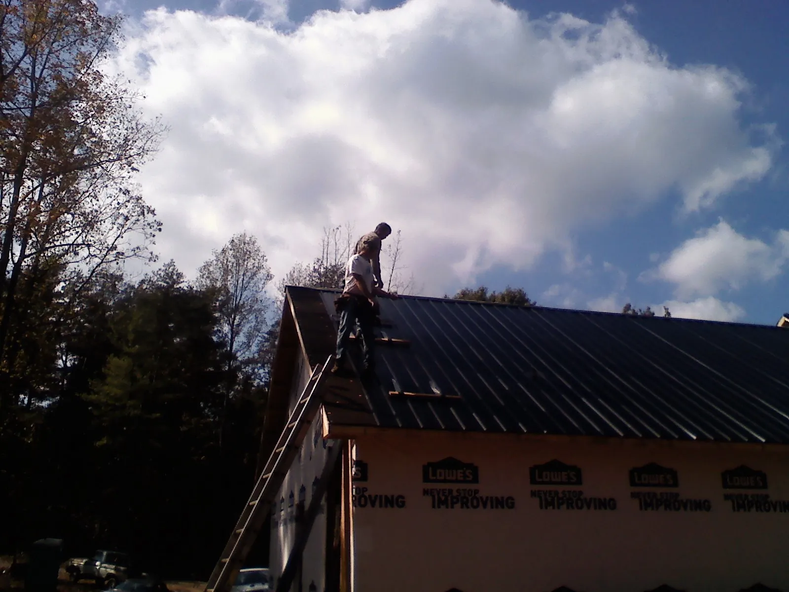 Roofer fastening dark metal panels high against a cloudy sky, from a Roof Inspection job in Marthasville