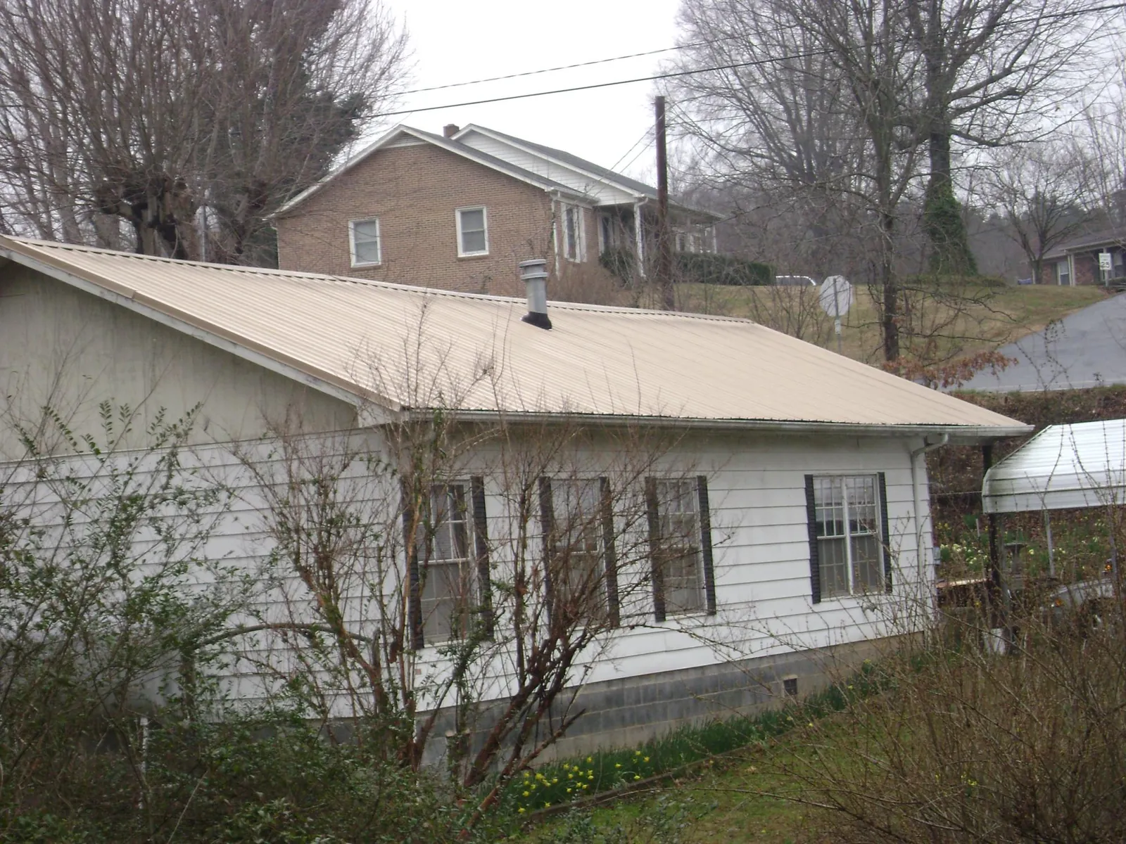 Tan metal roof on a white sided house set into a hillside — Commercial Roofing by Roofing Brothers in Marthasville