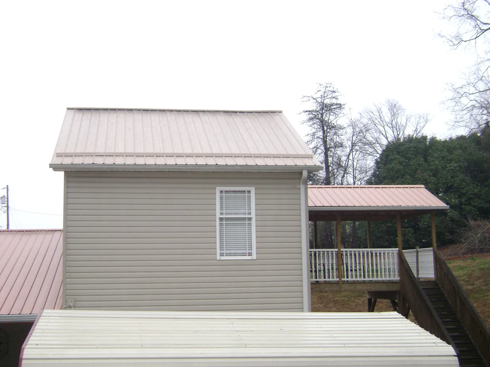 Tan metal roofs on a two story addition and attached porch, from a Roof Replacement job in Marthasville